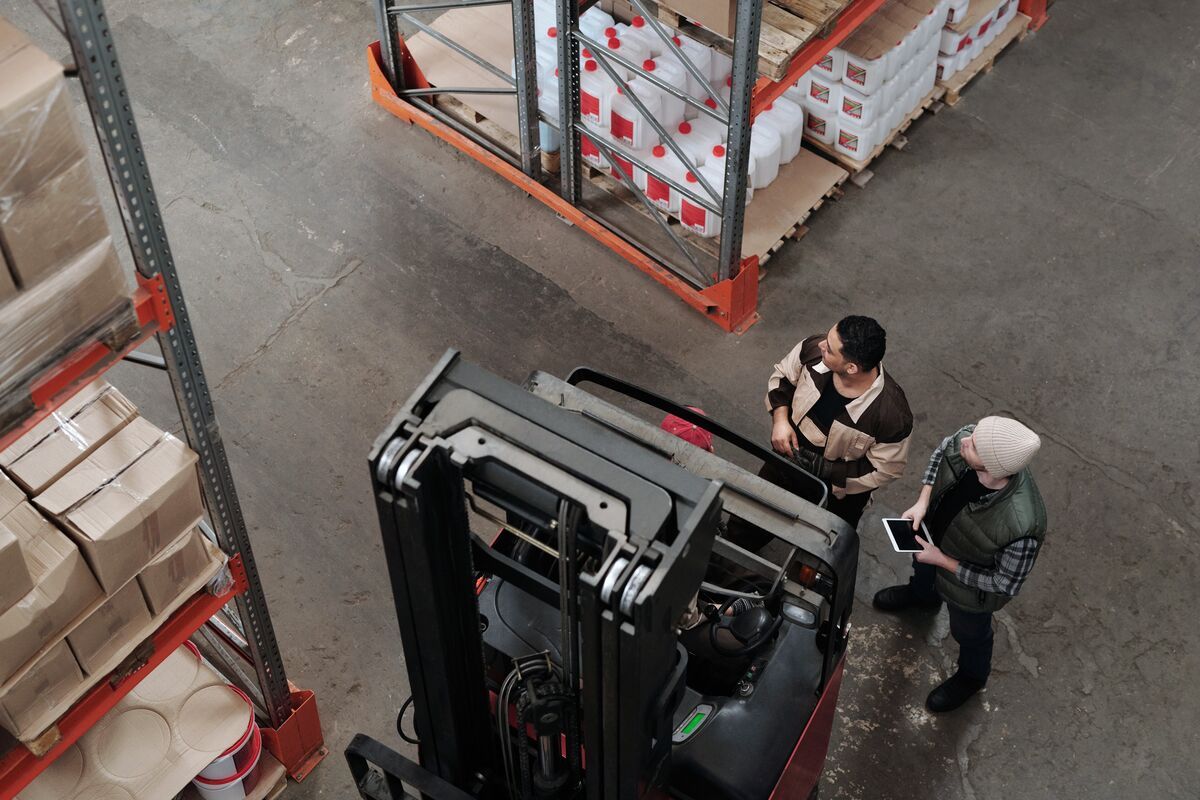An overhead view of a forklift beside tall storage racks and people checking information in a warehouse.