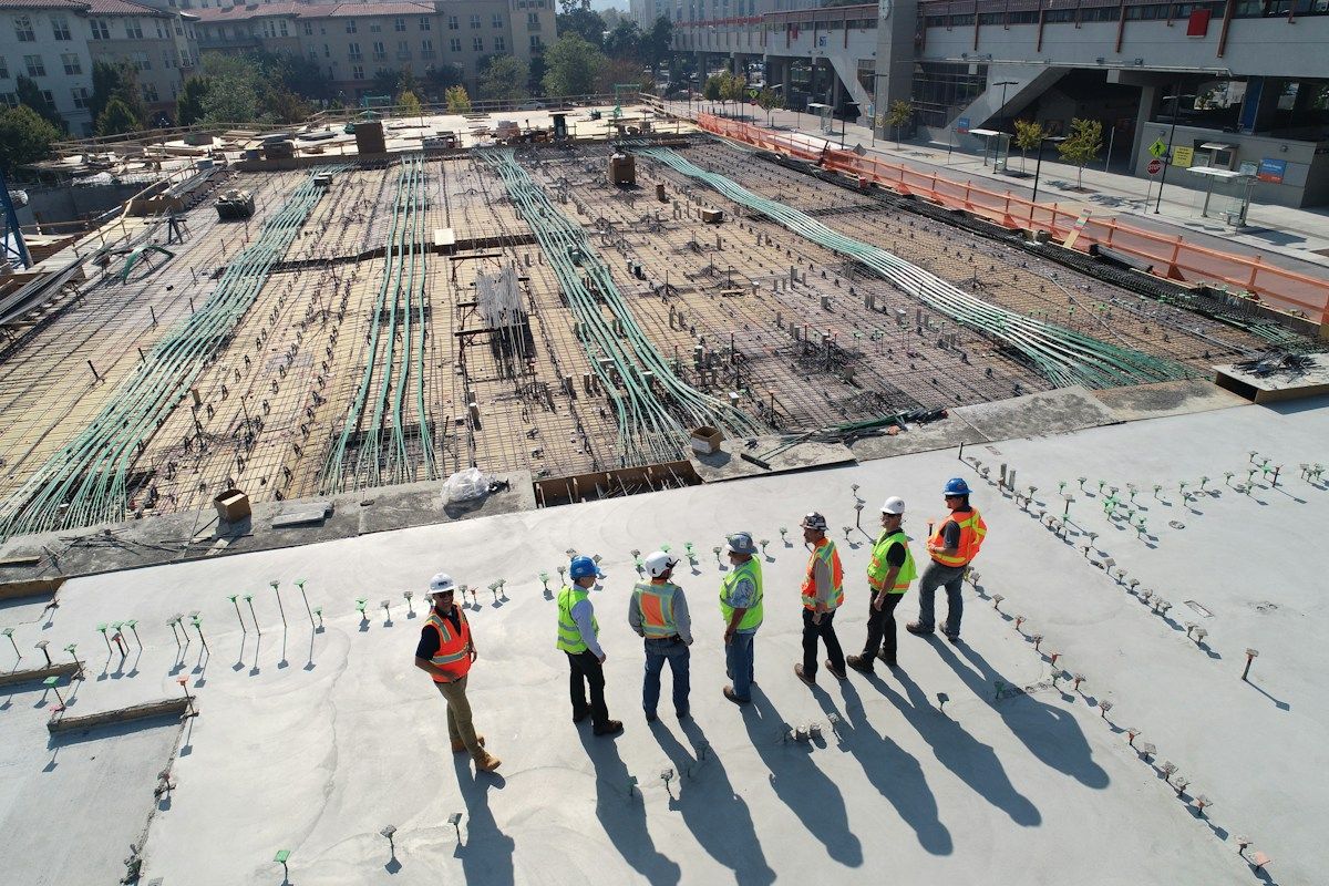 People wearing hard hats and high-visibility vests beside reinforcement work on a construction site.